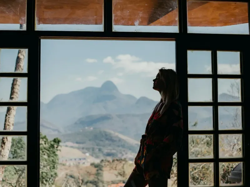Une femme respire face à une grande fenêtre ouverte sur des montagnes, le regard porté au loin