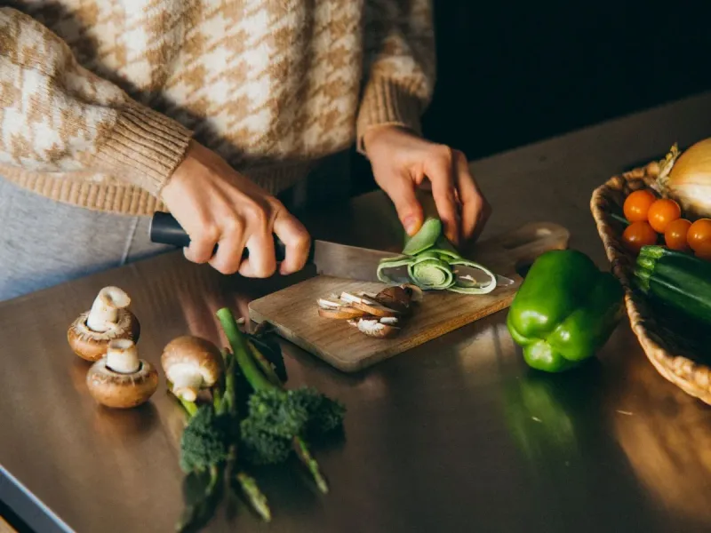 Des mains tranchent des légumes frais sur une planche en bois, dans une lumière douce