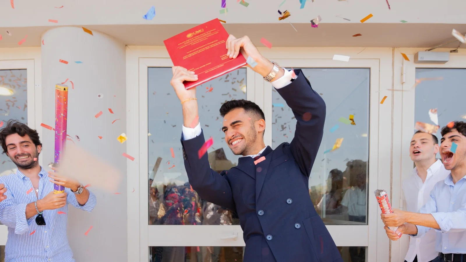 Un jeune diplômé brandit son mémoire au-dessus de sa tête sous une pluie de confettis, entouré d'amis
