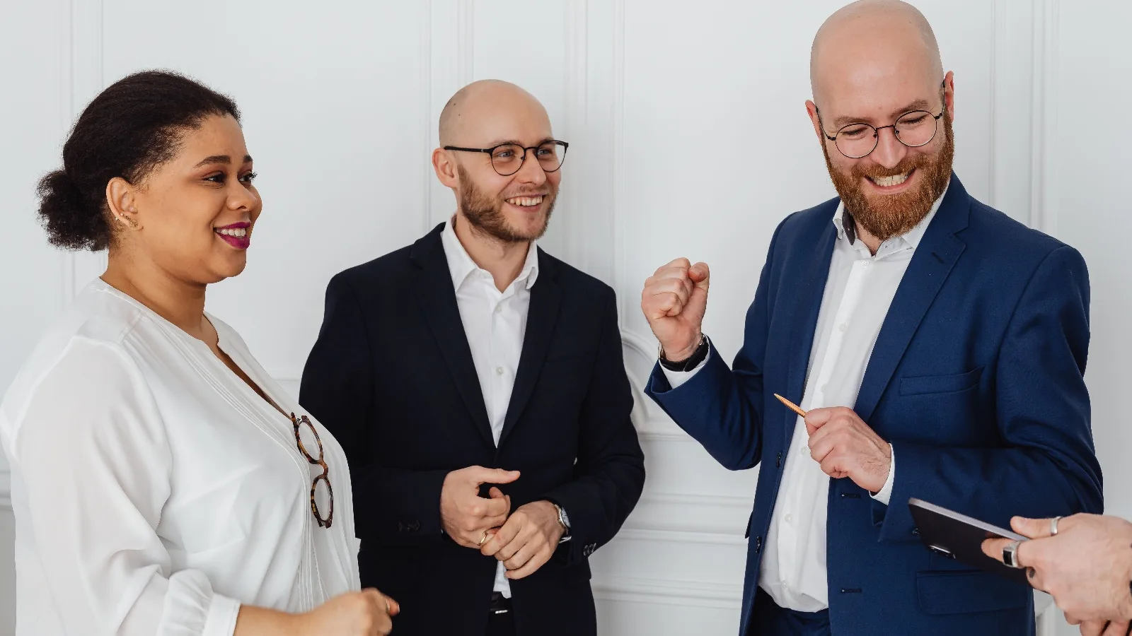 Trois personnes en tenue de travail, souriantes, l'une serrant le poing en signe de réussite