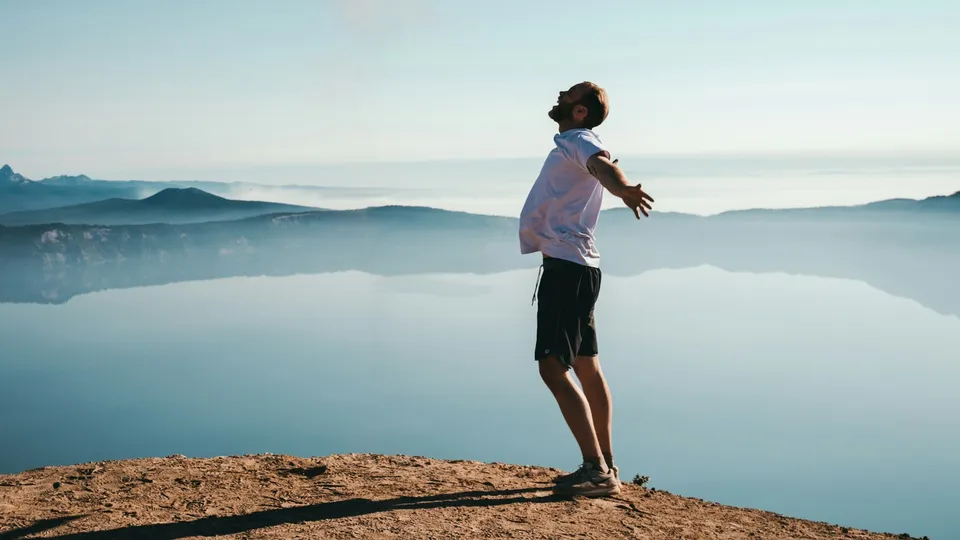 Un homme debout face à un lac, bras ouverts, qui respire librement
